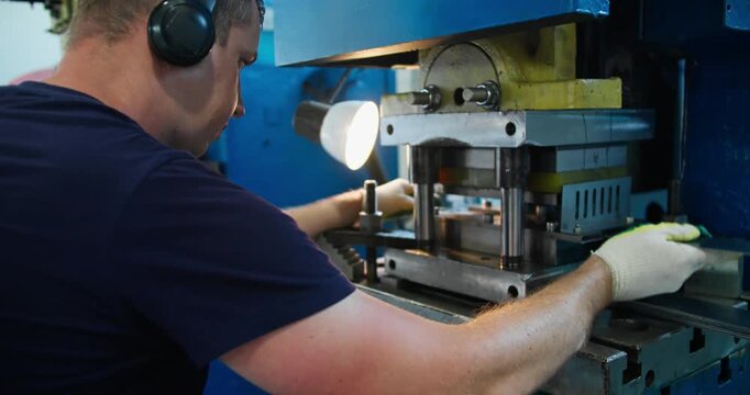 Blue-collar factory operator working at metal press machine in industrial workshop