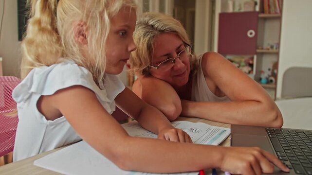 Mother helps her daughter complete school tasks using a laptop. Back to school concept with technology in family education