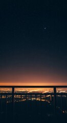 Fototapeta premium A metal balcony railing overlooks a dark expanse of glowing stars and soft city lights, creating a quiet atmosphere of late night solitude, stars, evening, shadow