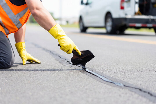 Construction worker sealing asphalt cracks on road surface