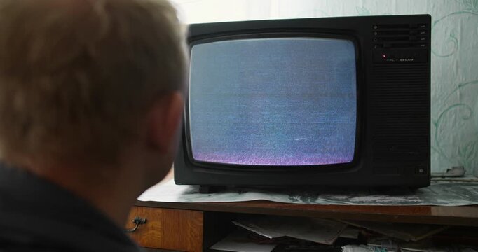Man watching CRT TV static, close-up from behind. Mindless viewing and media hypnosis concept