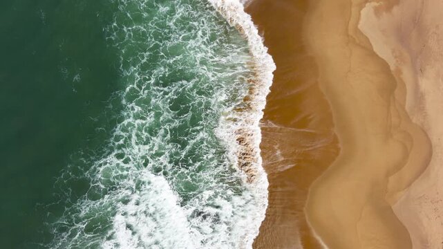 Top down, drone view of waves breaking in the sand with strong colours and beautiful patterns.