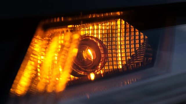 Car indicator light blinking on and off in close up, modern vehicle lighting detail, amber signal illumination, safety feature, night driving, automotive technology.