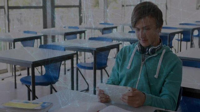 Male student glancing down at white tablet, leaning forward and smiling while studying in classroom