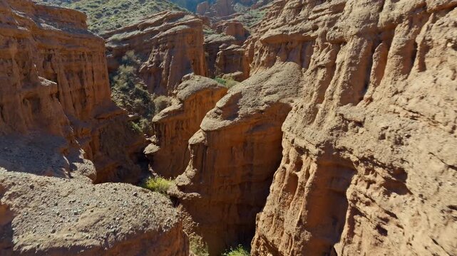 Aerial view captures stunning geological formations and eroded canyon walls in Kyrgyzstan. Serene landscape features rocks and sparse vegetation under bright blue sky.