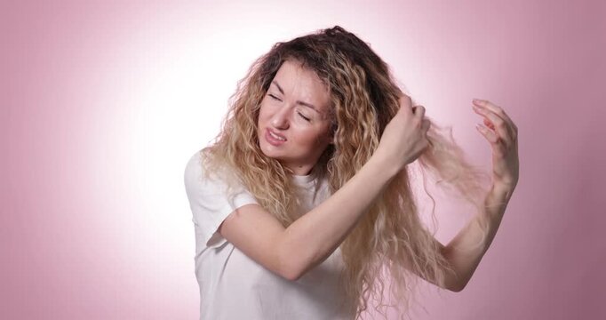 Unhappy woman trying to brush her tangled hair on pink background