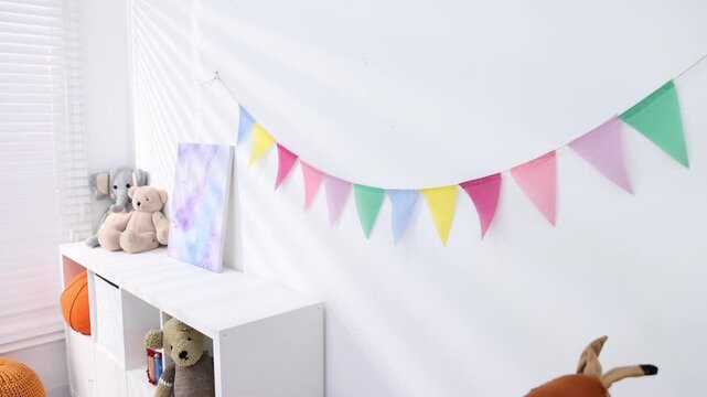 Colorful flags hanging on white wall in stylish child's room, camera moving forward. Interior design