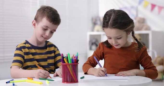 Cute little kids drawing with felt tip pens at white table indoors