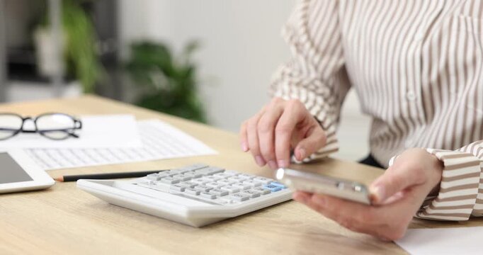 Budget planning. Woman with phone using calculator at wooden table indoors, closeup