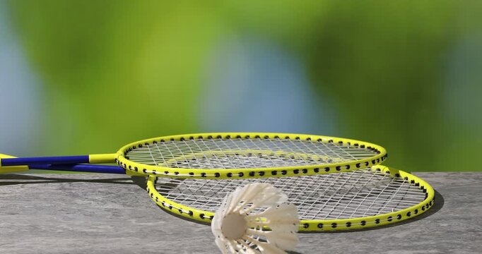 Shuttlecocks falling onto badminton rackets on light grey wooden table against blurred green background, closeup