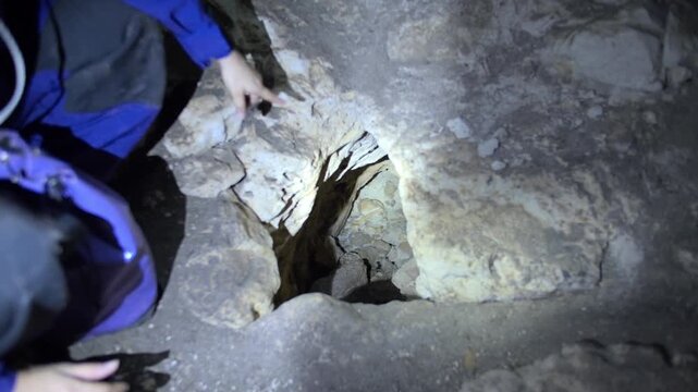Woman cavers illuminating a small underground passage inside a dark cavern with a flashlight