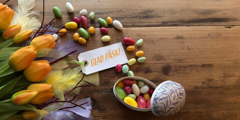 Glad Påsk Swedish Easter greeting tag with traditional candy and tulips on rustic wooden table, festive spring scene © LenaLensLife