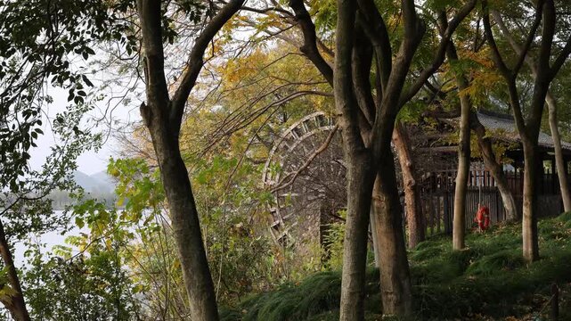 Traditional wooden water wheel nestled among autumn trees next to a peaceful lake.
