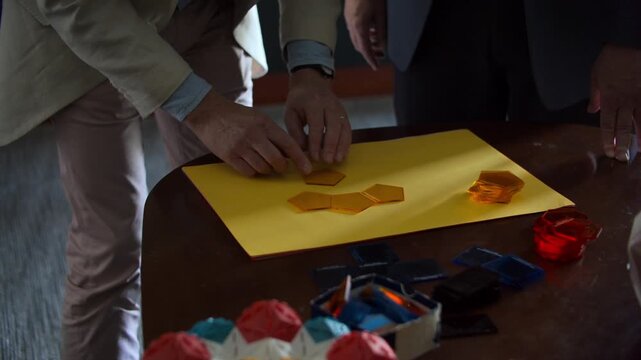 Colleagues collaborating on a project by arranging colorful plastic pentagons on a yellow paper