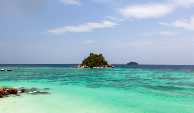 Ko Usen Islet view from Ko Lipe beach. Turquoise waters meet rocky shores under a clear sky. Tropical island landscape in Thailand.