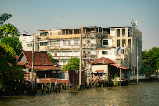Traditional wooden houses on stilts along the river with old concrete buildings in Bangkok, Thailand.