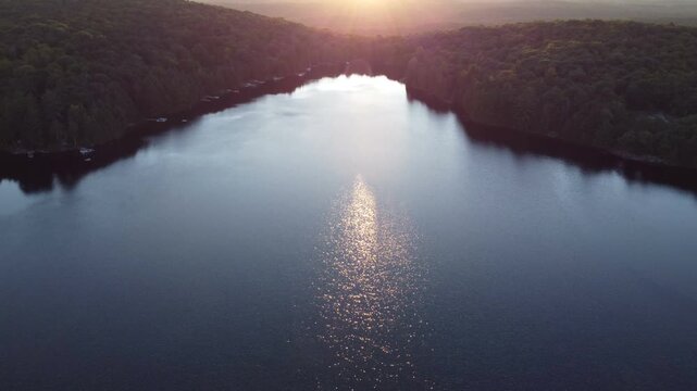 Aerial over Buckskin Lake into the sun with lens flare on a summer afternoon sunset. Lakeside cottages along side expansive wilderness of crown land located in the Tory Hill, Halliburton Highlands.
