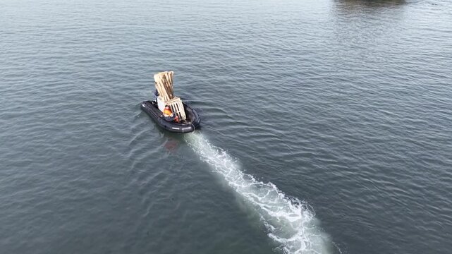 High-angle aerial of an inflatable Zodiac boat carrying wooden pallets and equipment from Fedor Konyukhov's dismantled solo station at Elephant Point back to the expedition ship