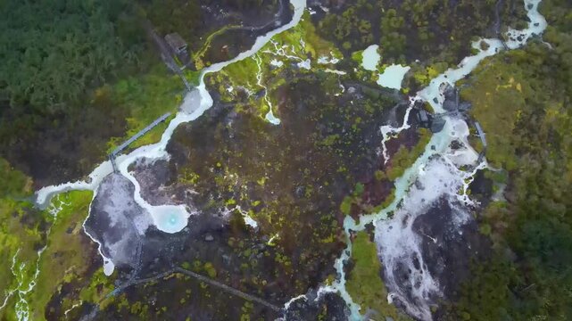 Drone overhead of milky turquoise pools and white mineral terraces linked by a wooden boardwalk, edged by dense forest in the Purace thermal area near Popayan.