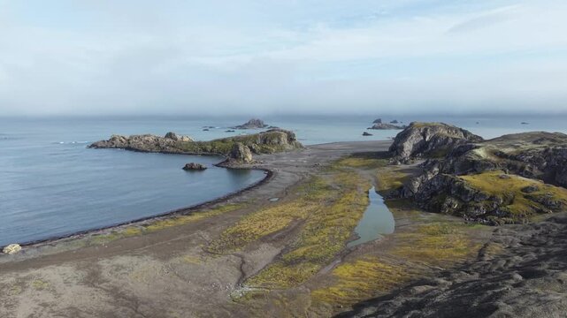 Aerial moves forward and tilts down to reveal a Russian team transferring dismantled materials from Fedor Konyukhov's solo station to Zodiac boats on the volcanic shores of Antarctica