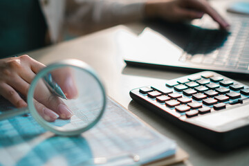 financial documents with calculator, pen and magnifying glass on desk, representing accounting, audit, business analysis, tax calculation and data verification