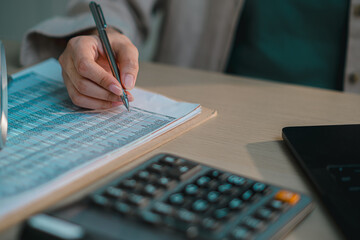 Close up of hand financial report with pen, calculator and laptop on desk, representing accounting, business analysis, budgeting, tax preparation and financial data management in modern office
