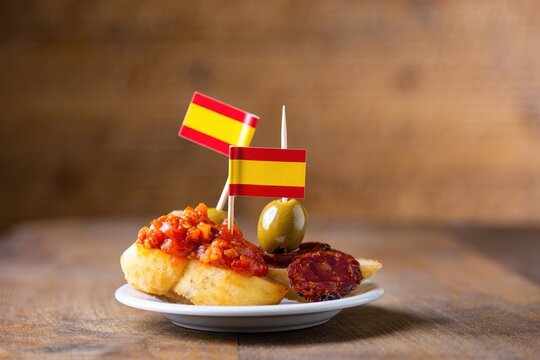 Spanish tapas plate with chorizo, olive and flag toothpick on rustic wood