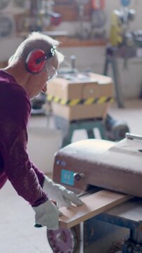 Senior carpenter sanding wooden plank in workshop