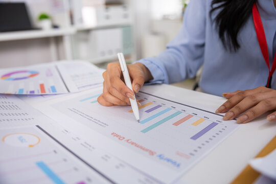Focused business person analyzing financial graph and chart on document in office using pen to review corporate strategy with deep concentration and attentive mood during busy workday