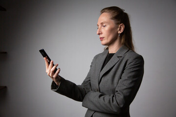 A profile portrait of a woman in a business suit standing and using a smartphone © vagon