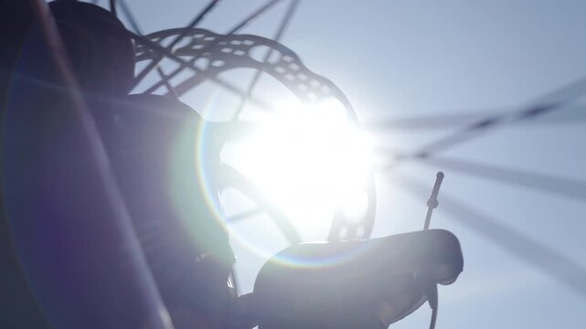 Close up of bicycle wheel with spokes and disc brake rotor against blue sky in sunlight. Concept of cycling equipment mechanics and active lifestyle.