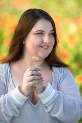 Portrait of a young woman inhaling the scent of a wildflower. Hands folded. Vertical photo. Body positivity.