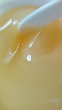 Close up of stirring thick yellow gel with spoon, bouncy chewy texture skincare product for healthy skin.