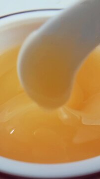 Close up of stirring orange gel with spoon, thick bouncy texture skincare product on clean background.