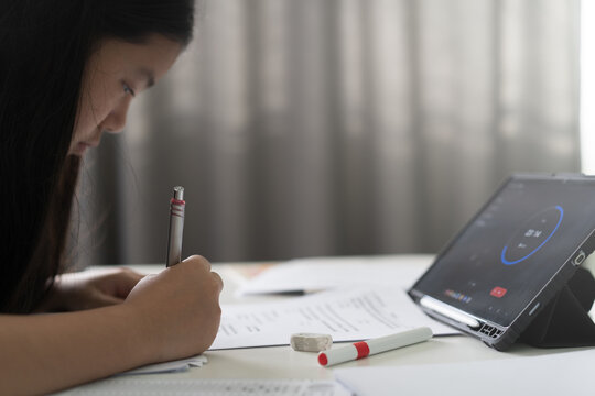 closeup hand child learn from home write on paper or young kid girl student doing homework taking test exam and being timed on computer tablet by study online class or people back to school learning