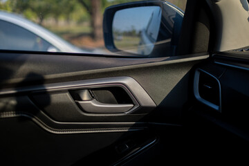 Obraz premium Modern Car Interior Door Handle and Side Mirror Close-up,Close-up shot of a modern car's interior door panel featuring a stylish black door handle, textured dashboard, and a view of the side-view.