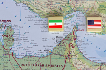 Naklejka premium American and Iranian flags on a plastic blocks near the Strait of Hormuz on a map, close-up.
