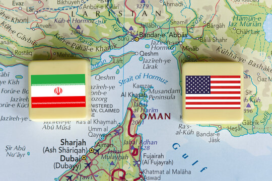 American and Iranian flags on a plastic blocks near the Strait of Hormuz on a map, close-up.