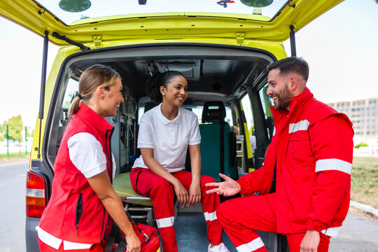 Group of paramedics talking at the back of an ambulance. Smiling diverse team of emergency medical responders discussing work during a break. Professional healthcare staff in uniform at a vehicle.