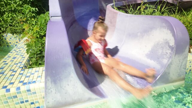 Happy girl riding down the slide in the waterpark. Little girl at water park. Fun on the water. Summer vacation