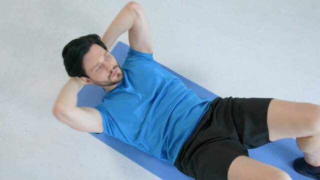 Top view of motivated active sporty fitness man practicing sit-ups exercise, flexing abs, strengthening back and hip muscles while doing sports training at home.