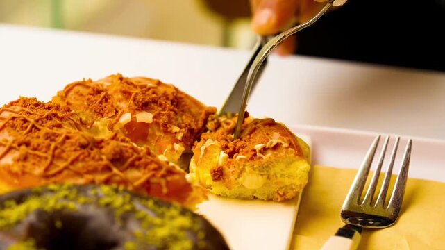 Cutting Dubai-style donuts with chocolate glaze, topped with chopped pistachios