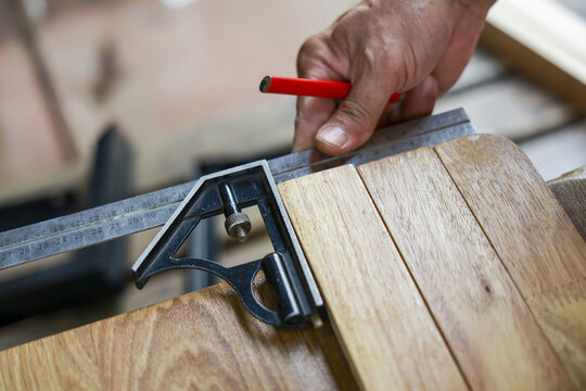 Focused carpenter hand using combination square tool to precisely measure and mark line on wood plank. skilled craftsman at work woodworking in his busy workshop
