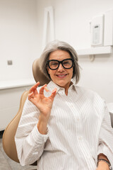 Happy senior woman smiling and holding a partial denture, showing successful dental treatment in a modern stomatology clinic