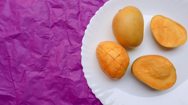 Top view of ripe yellow mango on plate with pink background. Juicy mangoes served eaten. Tasty yellow ripe mangoes