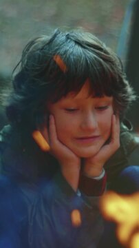 Child observes glowing flames, Young boy gazes at crackling fire, Young camper reflects awe by luminous campfire