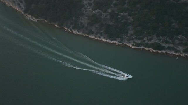 Aerial View of Speedboat Cruising Along Rocky Coastline Leaving White Foam Wake