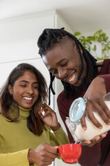 Couple African American and Indian pouring powder from glass jar into red cup at kitchen counter © wavebreak3