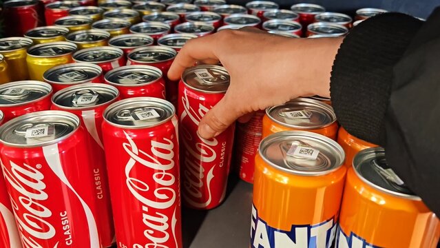 Belarus, Svetlogorsk, March 22, 2026. customer takes a can of cola from the supermarket fridge. female hand of a white girl takes a metal can. Buying soda in a supermarket store.