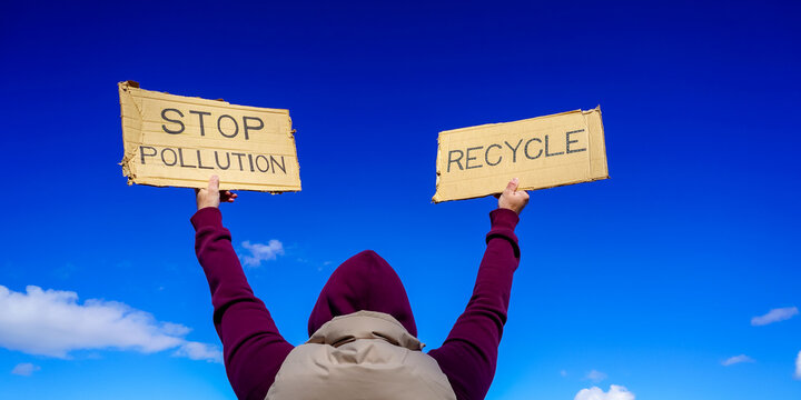 Activist holding stop pollution and recycle signs  under a blue sky